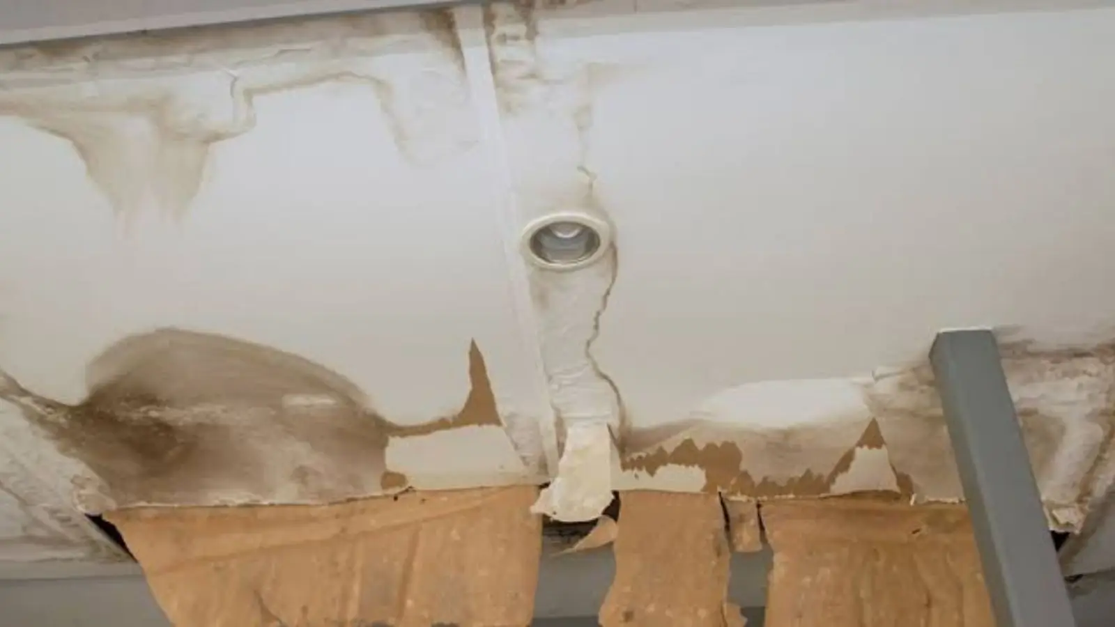 Water-stained ceiling around a light fixture with sagging, discolored drywall