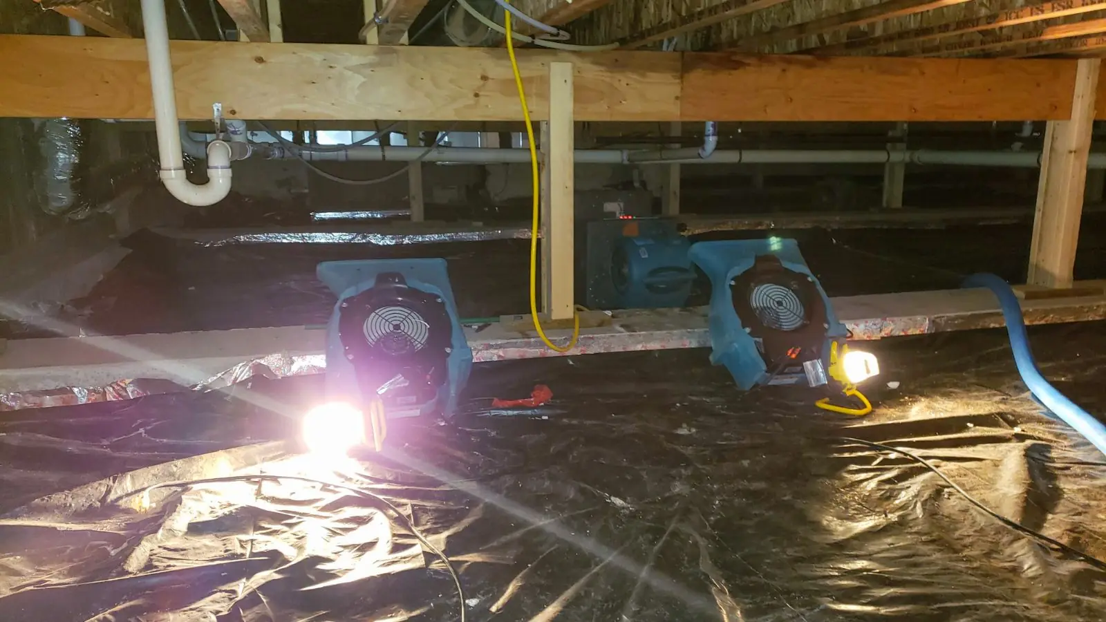 Crawl space lined with plastic sheeting and an air mover under floor framing