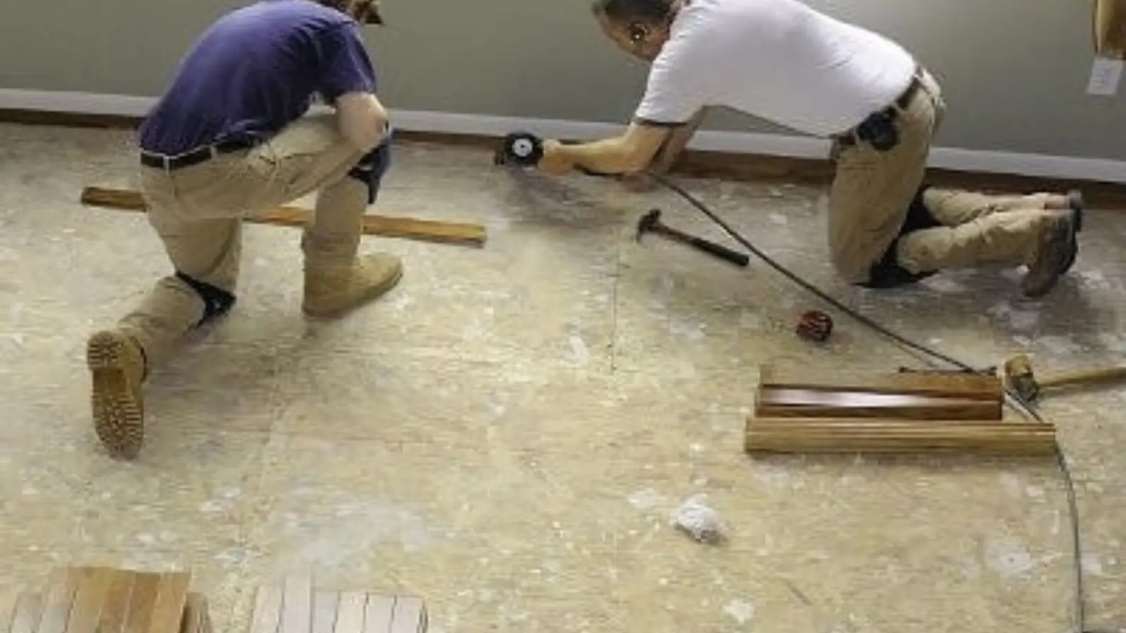 Two workers fitting replacement floor planks during a water damage repair