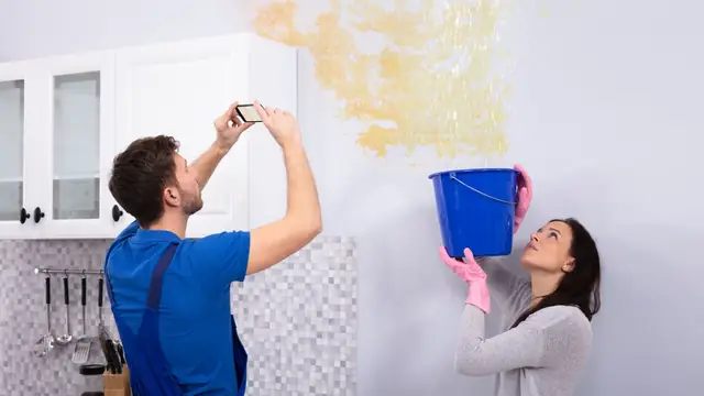 Homeowners looking at a ceiling water stain with a bucket catching drips
